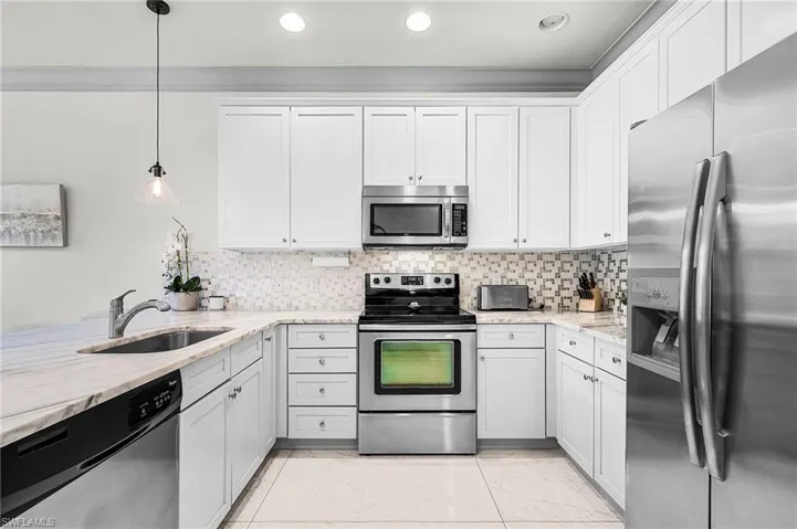 Kitchen with appliances with stainless steel finishes, decorative light fixtures, light stone countertops, backsplash, and recessed lighting