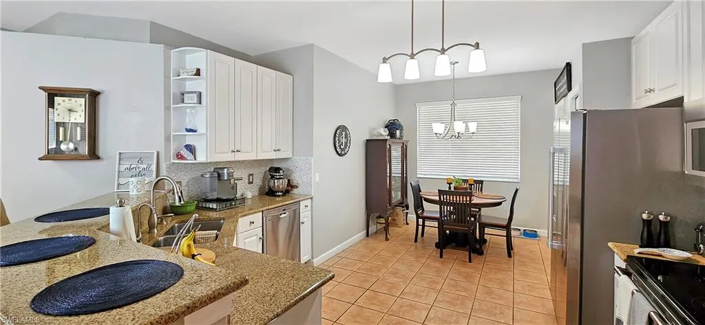 Kitchen with appliances with stainless steel finishes, open shelves, light stone countertops, decorative backsplash, and a sink