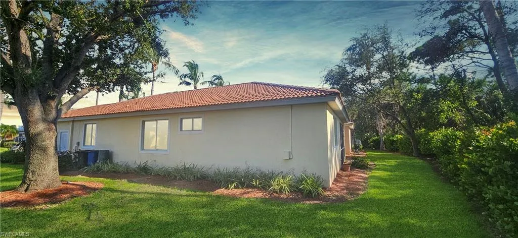 View of property exterior with a yard, stucco siding, and a tiled roof