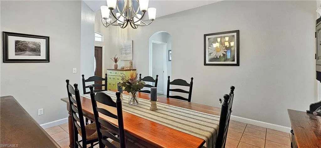 Dining space with arched walkways, light tile patterned floors, baseboards, and an inviting chandelier