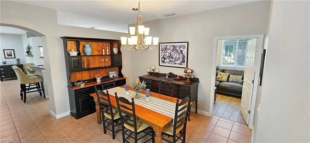 Dining area featuring baseboards, a chandelier, light tile patterned floors, visible vents, and arched walkways