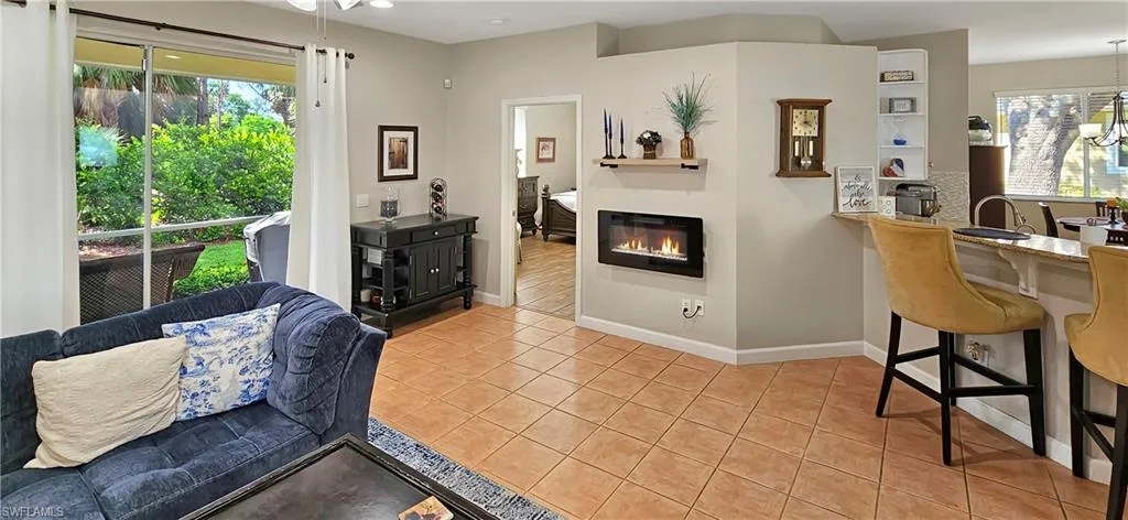 Living area with a healthy amount of sunlight, light tile patterned floors, baseboards, and a glass covered fireplace