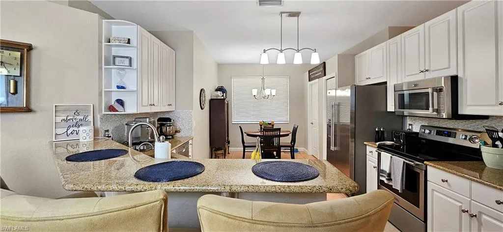 Kitchen featuring stainless steel appliances, white cabinets, an inviting chandelier, and open shelves