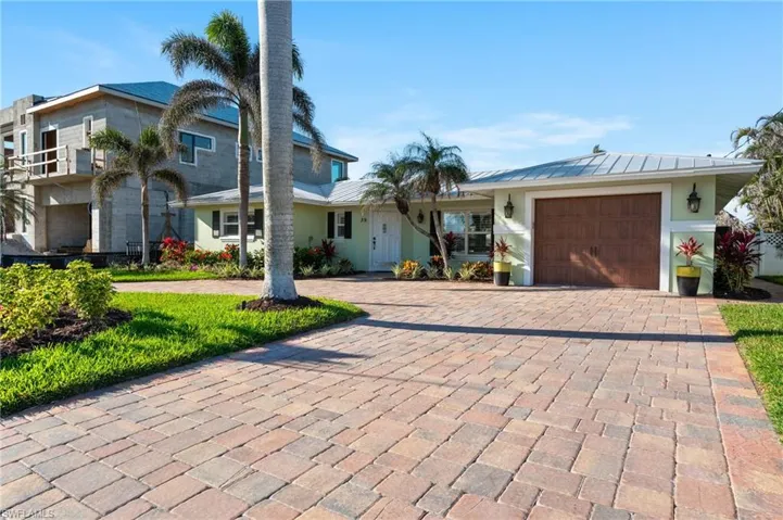 View of front of property featuring decorative driveway, an attached garage, a standing seam roof, and metal roof. virtually enhanced image