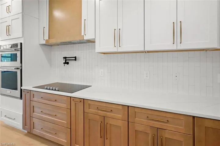 Kitchen featuring tasteful backsplash, double oven, light stone countertops, and black electric cooktop