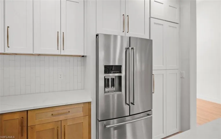 Kitchen with high quality fridge, light stone counters, white cabinetry, and wood finished floors