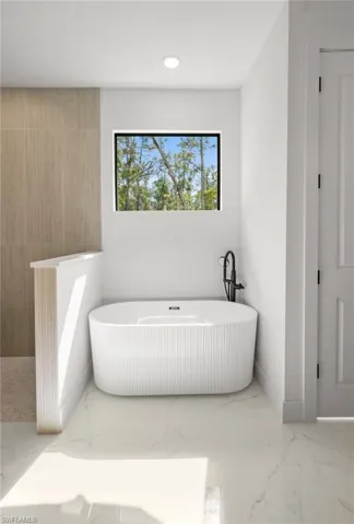 Full bathroom with light marble finish flooring, a freestanding tub, and recessed lighting