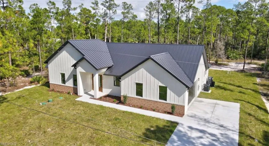 Modern farmhouse featuring a front lawn, brick siding, board and batten siding, and a metal roof
