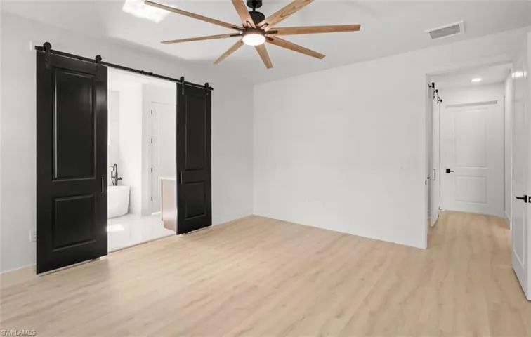 Unfurnished bedroom with a barn door, light wood-style flooring, a ceiling fan, and ensuite bath