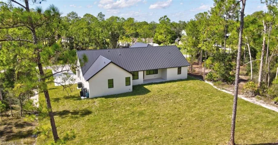 Back of property featuring a yard, a patio area, view of scattered trees, and a metal roof