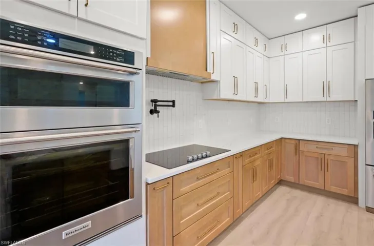 Kitchen with stainless steel appliances, tasteful backsplash, light wood-style flooring, recessed lighting, and light stone countertops