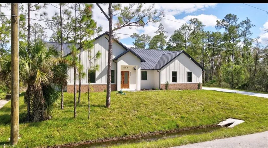 Modern farmhouse style home featuring board and batten siding, a front lawn, a standing seam roof, a metal roof, and brick siding