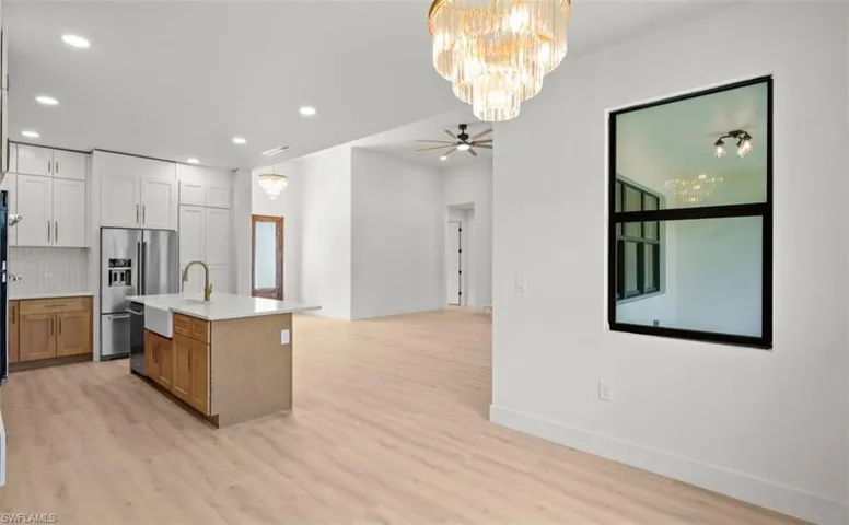 Kitchen with brown cabinetry, a chandelier, open floor plan, decorative light fixtures, and a center island with sink