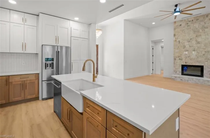 Kitchen with brown cabinets, an island with sink, open floor plan, high end fridge, and light wood-type flooring