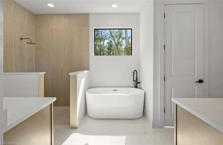 Full bath featuring vanity, a walk in shower, a freestanding tub, light marble finish flooring, and recessed lighting