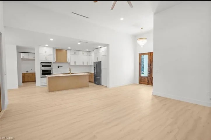 Kitchen with recessed lighting, open floor plan, a kitchen island with sink, light wood finished floors, and white cabinets