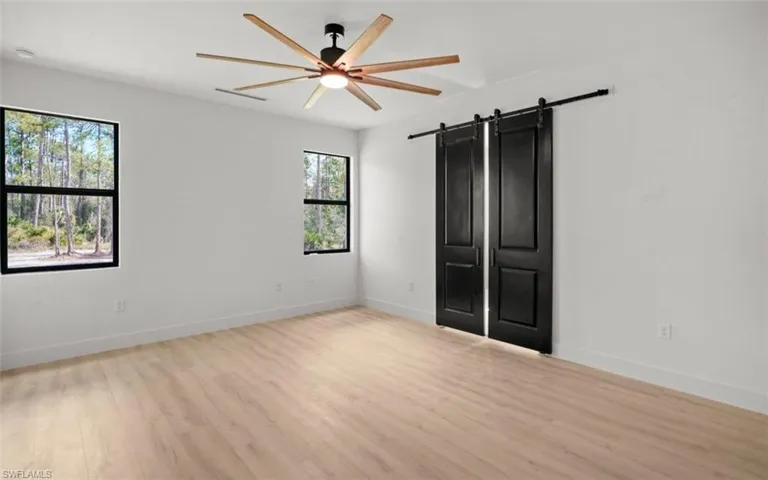 Unfurnished bedroom featuring a barn door, light wood-style flooring, and ceiling fan