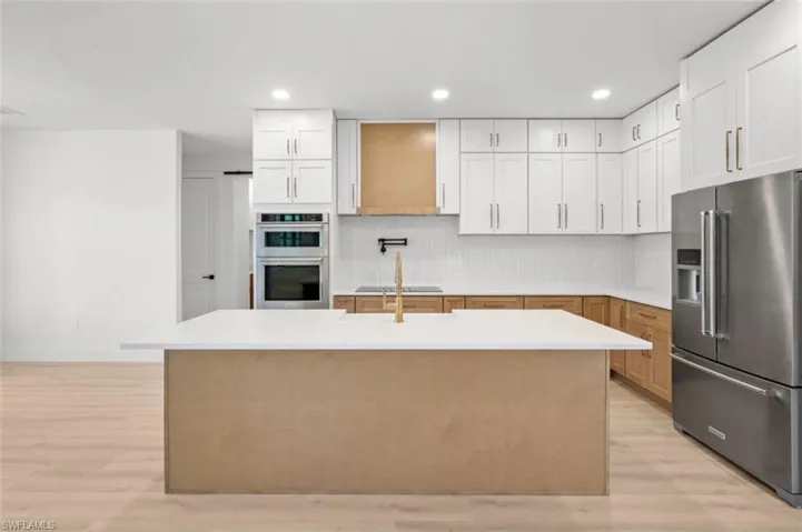 Kitchen featuring appliances with stainless steel finishes, white cabinetry, light wood-style flooring, a center island with sink, and recessed lighting