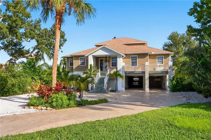 Elegant two-story residence showcasing a stucco exterior with tile roof, elevated on pilings with a two-car garage beneath - Virtually Edited Image