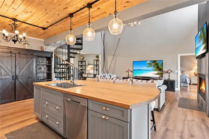 Wood-finish flooring throughout, vaulted wood-paneled ceiling, kitchen island with wood countertop, built-in stainless steel dishwasher, and spiral staircase - Virtually Edited Image