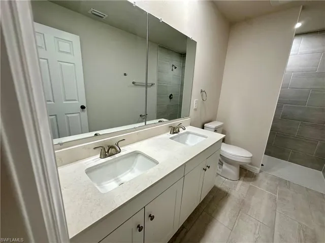 Full bath featuring tiled shower and double vanity