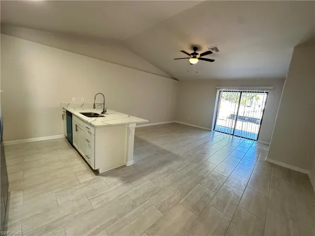 Kitchen featuring a peninsula, white cabinetry, ceiling fan, light stone countertops, and open floor plan