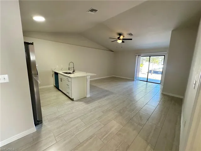Kitchen featuring a peninsula, a ceiling fan, freestanding refrigerator, white cabinets, and lofted ceiling