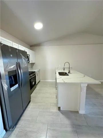 Kitchen featuring stainless steel appliances, white cabinets, light stone counters, a peninsula, and lofted ceiling