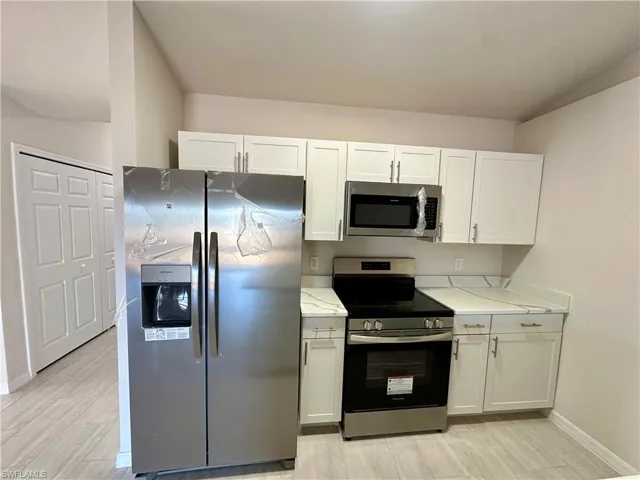Kitchen with stainless steel appliances, white cabinetry, light wood-style flooring, and light stone countertops