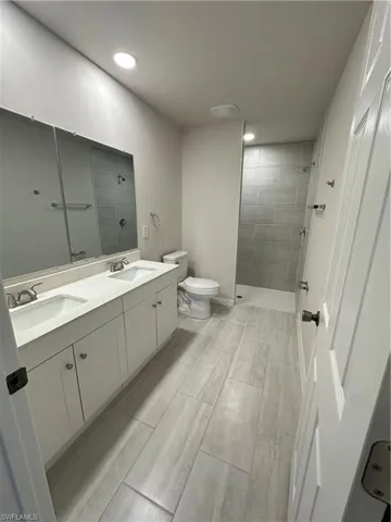 Bathroom with double vanity, tiled shower, wood finish floors, and recessed lighting