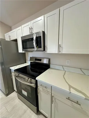 Kitchen featuring stainless steel appliances, white cabinetry, light stone countertops, and light wood-style floors