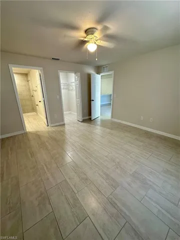 Unfurnished bedroom with a ceiling fan, ensuite bathroom, and a spacious closet