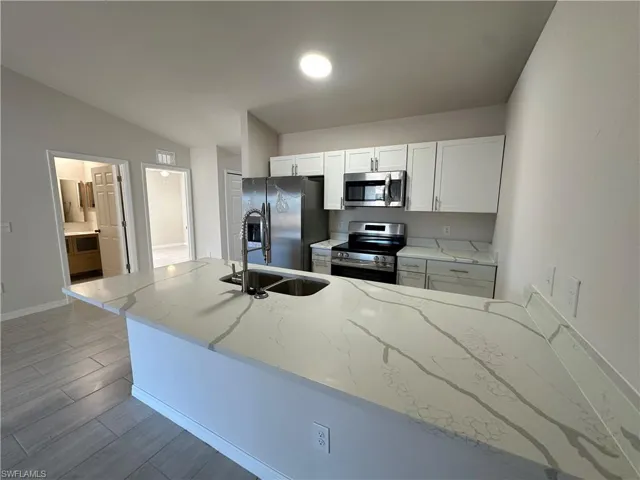 Kitchen with a peninsula, white cabinets, stainless steel appliances, wood tiled floors, and light stone countertops