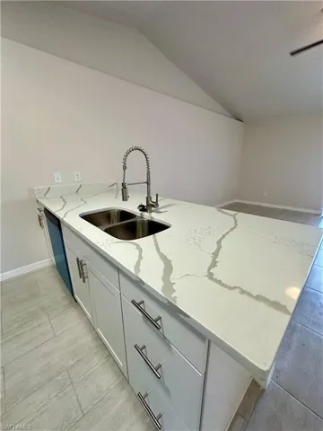 Kitchen with light stone counters, a peninsula, light wood-type flooring, white cabinets, and vaulted ceiling