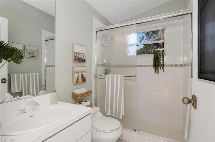 Bathroom featuring an enclosed shower, vanity, vaulted ceiling, and toilet