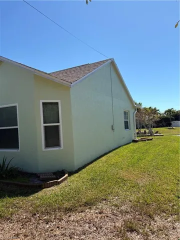 View of side of property with a yard, stucco siding, and roof with shingles