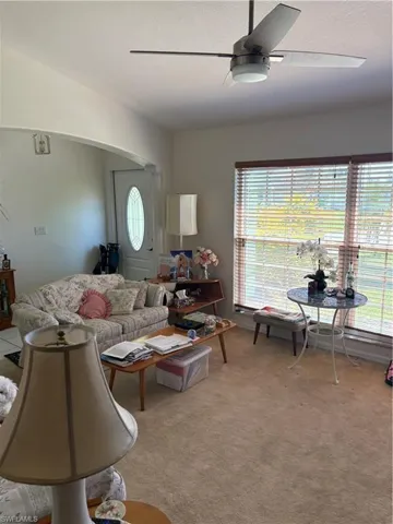 Living area featuring ceiling fan, arched walkways, light carpet, and a textured ceiling