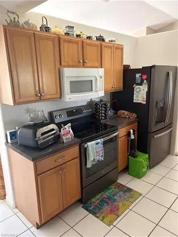 Kitchen featuring stainless steel electric range, wood finish cabinets, dark countertops, light tile patterned floors, and refrigerator
