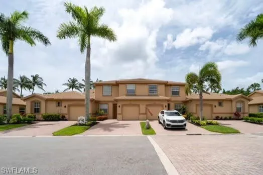 Tan stucco exterior with a dual-pitch roof, integrated garage, and a paver driveway