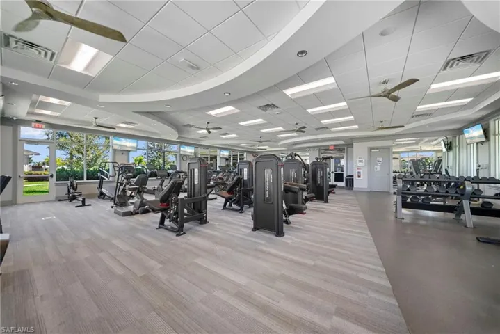 Fitness center with multiple exercise machines, weight rack, ceiling fans, and large windows