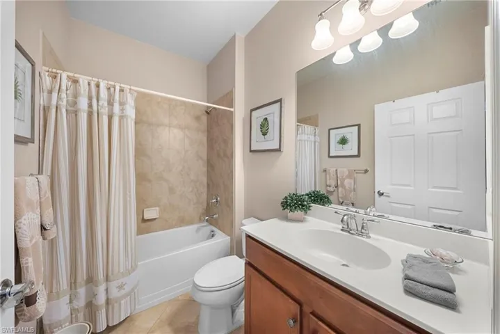 Bathroom featuring a vanity with a white countertop and wood-finish cabinetry, a built-in bathtub with tiled surround, and a wall-mounted light fixture