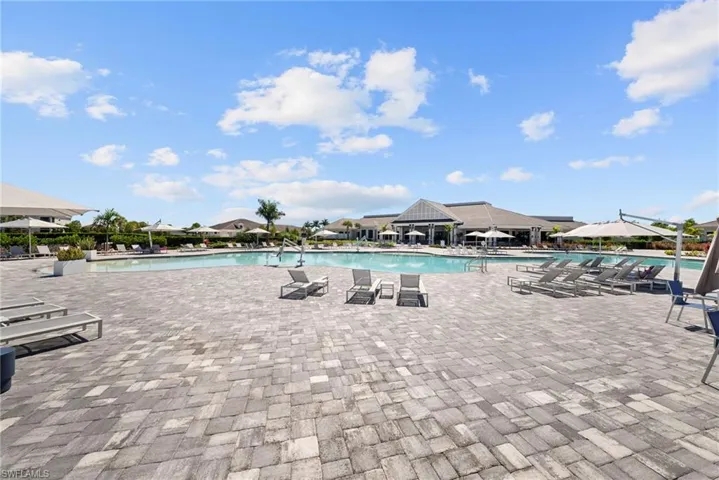 Expansive paver patio with a large swimming pool and a prominent clubhouse building