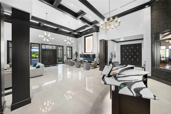 Spacious lobby featuring polished tile flooring, coffered ceiling details, a modern chandelier, and a decorative reception desk