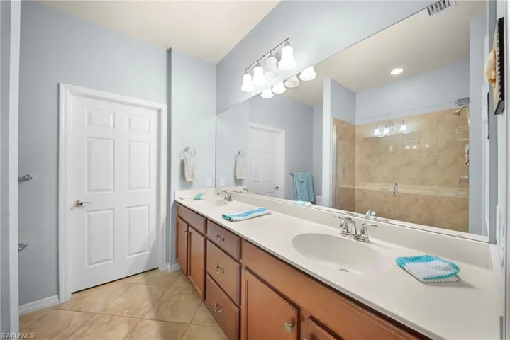 Dual vanity with integrated sinks, wood-finish cabinetry, full-width mirror, and a glass-enclosed shower with tiled walls