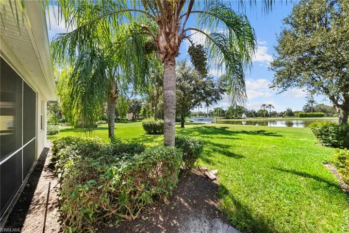 Screened patio with a covered soffit, surrounded by lush landscaping, mature palm trees, and a grassy lawn overlooking a body of water