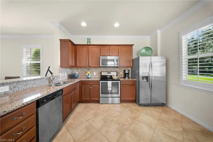 Kitchen featuring wood cabinetry, stainless steel appliances, granite countertops, tile flooring, and plantation shutters