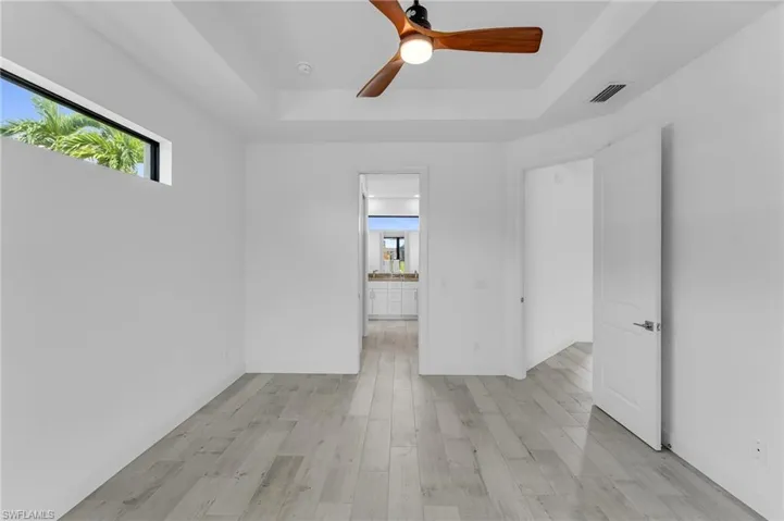 Spare room with ceiling fan, light hardwood / wood-style floors, and a tray ceiling