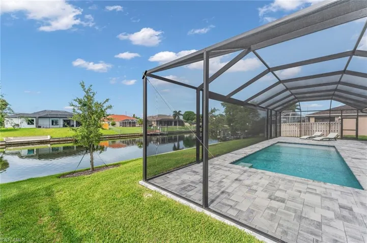 View of swimming pool featuring a patio area, a lawn, glass enclosure, and a water view