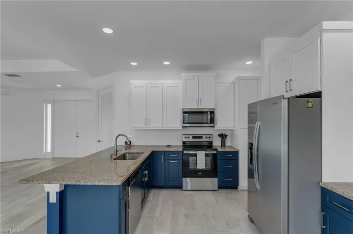 Kitchen with blue cabinets, stainless steel appliances, sink, light hardwood / wood-style flooring, and kitchen peninsula