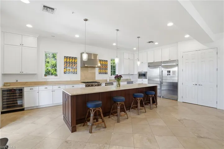 Dual tone kitchen featuring two tone color scheme, pendant lighting, built in appliances, beverage cooler, and a spacious island
